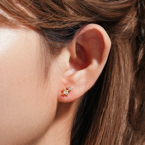 Detailed view of a gold star and circle stud earring set with zircons on a model's ear