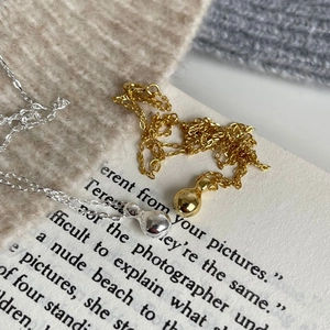 Close-up of minimalist teardrop pendants in gold and silver on a textured knit background