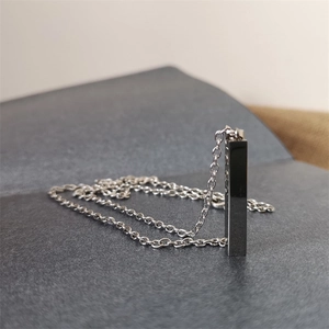 Close-up of a silver rectangular column pendant necklace on a dark textured surface