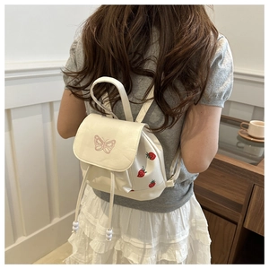 Detail of white butterfly embroidery and strawberry print on a small PU leather backpack