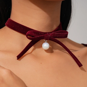 Detail of burgundy velvet choker with a plush bow and elegant hanging pearl pendant