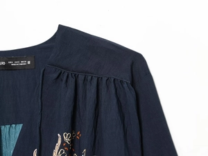 Gros plan détaillé des broderies florales et du décolleté sur cette blouse en crêpe bleu marine
