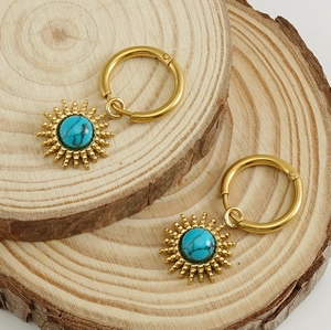 Detailed close-up of 18K gold plated sunburst earrings with turquoise stone on wood