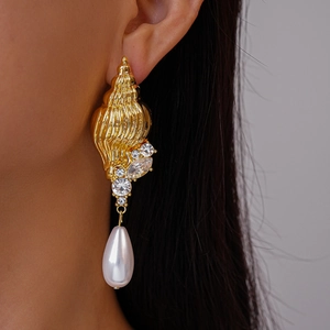 Detail of gold shell earrings with crystals and pearl pendants worn by a model