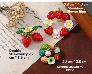 Close-up of cute strawberry enamel brooches with floral wreaths on vintage background