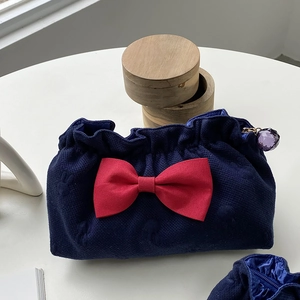 Detail of navy cosmetic bag with red bow, pleated closure, and purple crystal pendant