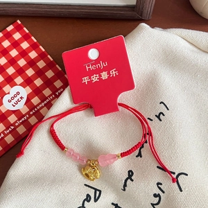 Detail of red braided lucky bracelet with pink beads and golden rat charm on canvas