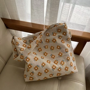 Minimalist beige canvas tote bag with orange floral embroidery on a chic leather chair