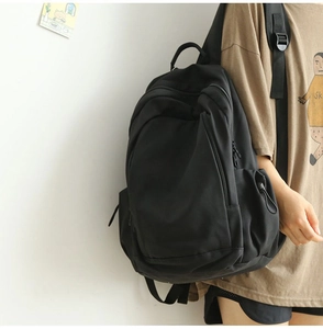 Side view of a minimalist black canvas backpack worn by a model against a white wall