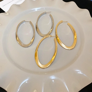 Macro detail of large chunky oval hoop earrings in polished gold and silver finishes