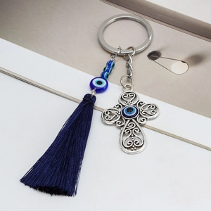 Detail of cross keychain with blue tassels and evil eye beads on white background