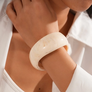 Close-up of minimalist cream resin bangle with brown marble texture worn by a model