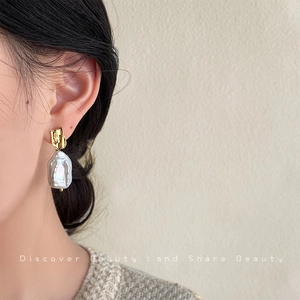 Close-up of elegant baroque pearl earrings with irregular gold metal studs on a model