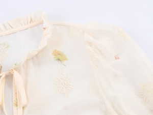 Detail of floral embroidery and ruffles on apricot French style tie-neck blouse