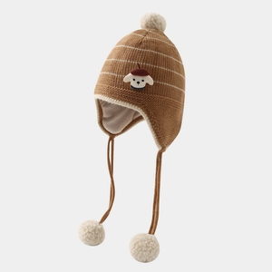 Detailed knit texture of a brown winter baby hat with soft white pom poms and dog embroidery