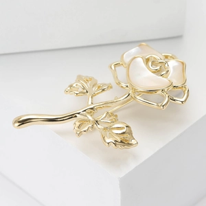 Macro view of shell rose flower brooch in gold finish on a white pedestal