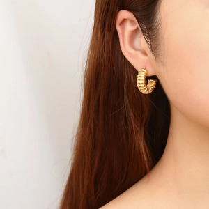 Macro shot of gold croissant-style C-shaped earrings with wave texture on female model