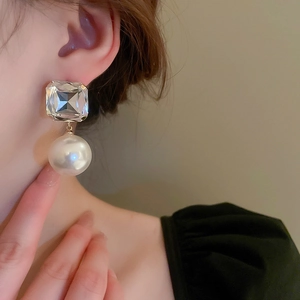 Close-up of elegant square crystal and pearl drop earrings worn by a model