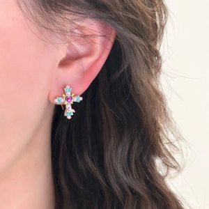 Close-up of a silver cross earring with colorful rhinestones worn by a model