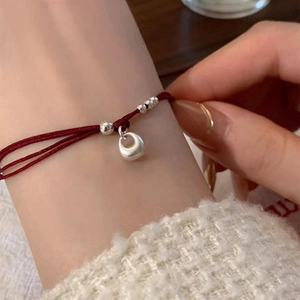 Close-up of a dark red cord bracelet with silver beads and pendant on a wrist