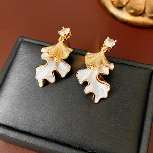Macro detail of leaf-shaped gold earrings with white enamel and sparkling zircon accents