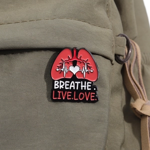 Detail of red lung enamel pin with heart monitor line on green canvas bag
