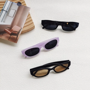 Three pairs of vintage cat-eye sunglasses in black, purple, and brown on a beige backdrop