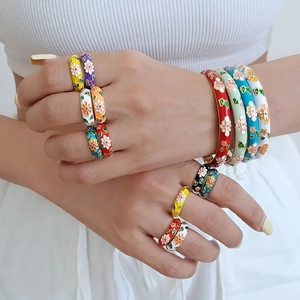 Detailed view of colorful enamel flower rings and matching bracelet worn by a model