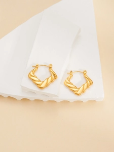 Detailed view of gold twisted hoop earrings with textured spiral design on stone surface
