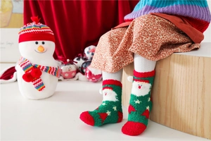 Close-up of green and red Christmas socks for kids with Santa Claus and white pom-pom detail
