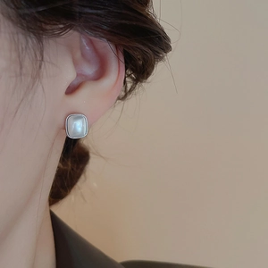Détail d'une boucle d'oreille carrée en argent avec incrustation d'opale sur l'oreille