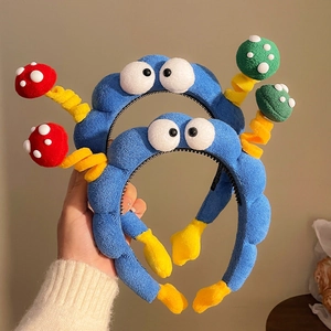 Dettaglio del cerchietto in peluche blu con grandi occhi 3D e decori a forma di fungo