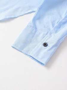 Detalle del puño de camisa de algodón azul claro con costura limpia y botón negro