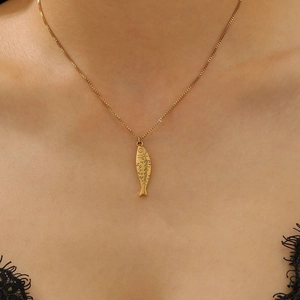 Detail of a minimalist gold stainless steel fish pendant necklace worn by a model