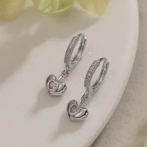 Boucles d'oreilles cœur argenté avec zircons roses et pavé de cristaux sur plat blanc