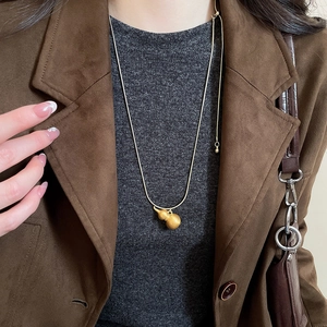 Dettaglio di una collana con ciondolo a zucca dorata spazzolata su una giacca di pelle scamosciata