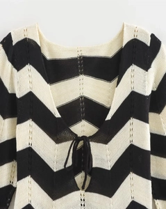 Détail d'un haut en tricot noir et blanc avec col à lacets et texture ajourée ondulée