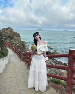 Detail of white off-shoulder ruffled top and embroidered lace maxi skirt on seaside