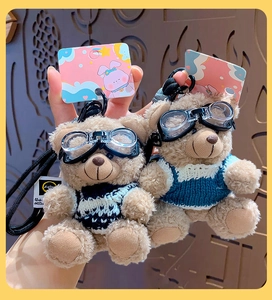 Close-up of a plush bear keychain wearing a knitted sweater and miniature goggles