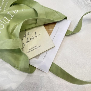 Close-up of light green canvas tote bag showing large capacity and artistic letter printing