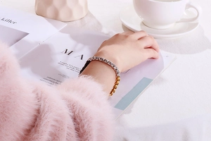 Detail of silver and gold tone square box chain bracelet worn on wrist with magazines