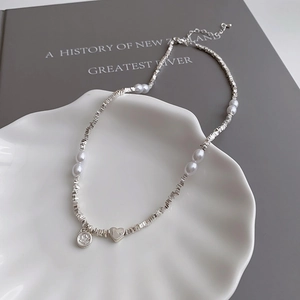 Macro view of silver chunky beads and pearls necklace with a heart pendant on a shell tray