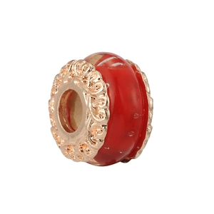 Detailed macro of red glass bead charm with golden hollow metal floral patterns