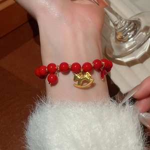 Detail of red beaded bracelet with a gold rocking horse pendant on a wrist