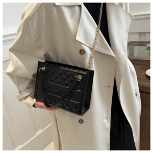 Detail of black quilted shoulder bag with FASHION embossing and gold chain strap