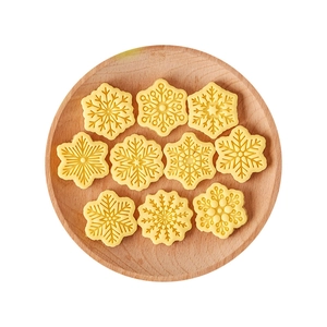 Ten yellow snowflake cookie shapes with detailed embossing on a round wooden tray