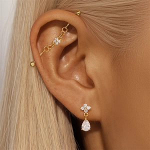 Detail of gold industrial barbell with flower motif and teardrop zircon studs worn by model