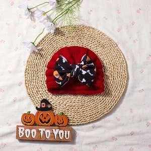 Detail of red knitted baby turban with large Halloween themed bow on straw mat