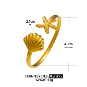 Golden stainless steel cuff bracelet featuring shell and starfish charms on a white background