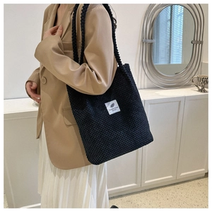 Detail of black textured corduroy tote bag worn by a model in a minimalist blazer